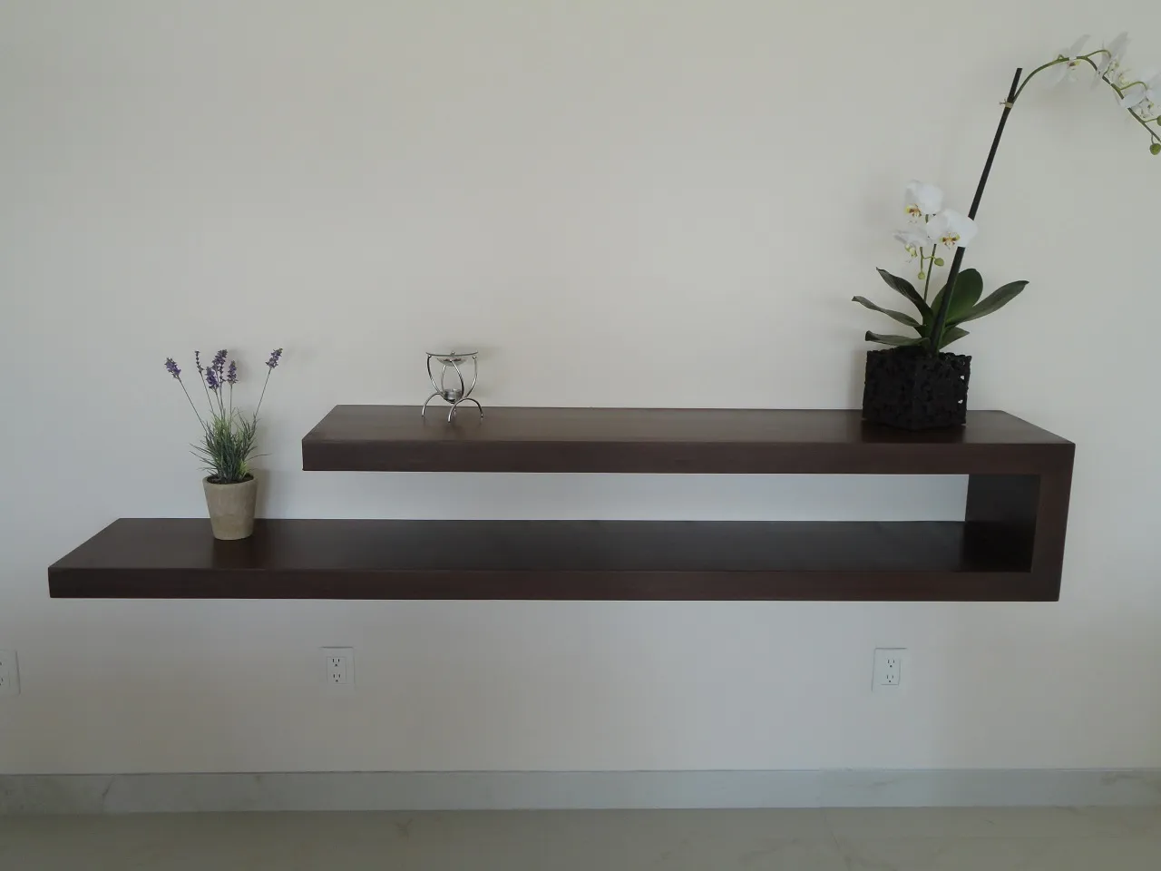 Consola suspendida de madera oscura sobre muro blanco, con una orquídea encima.