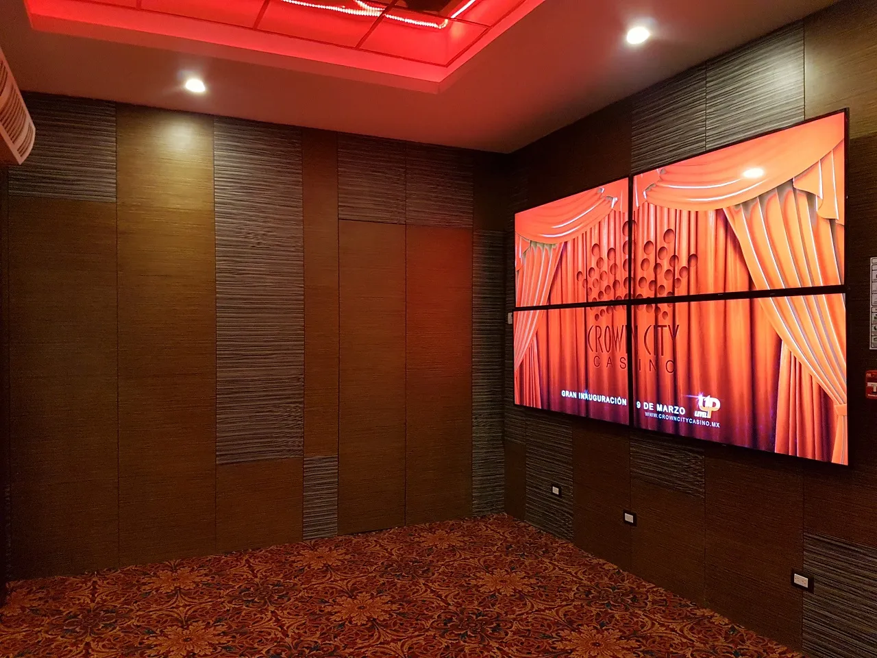 Sala con muro de madera y videowall, con plafón e iluminación en rojo.