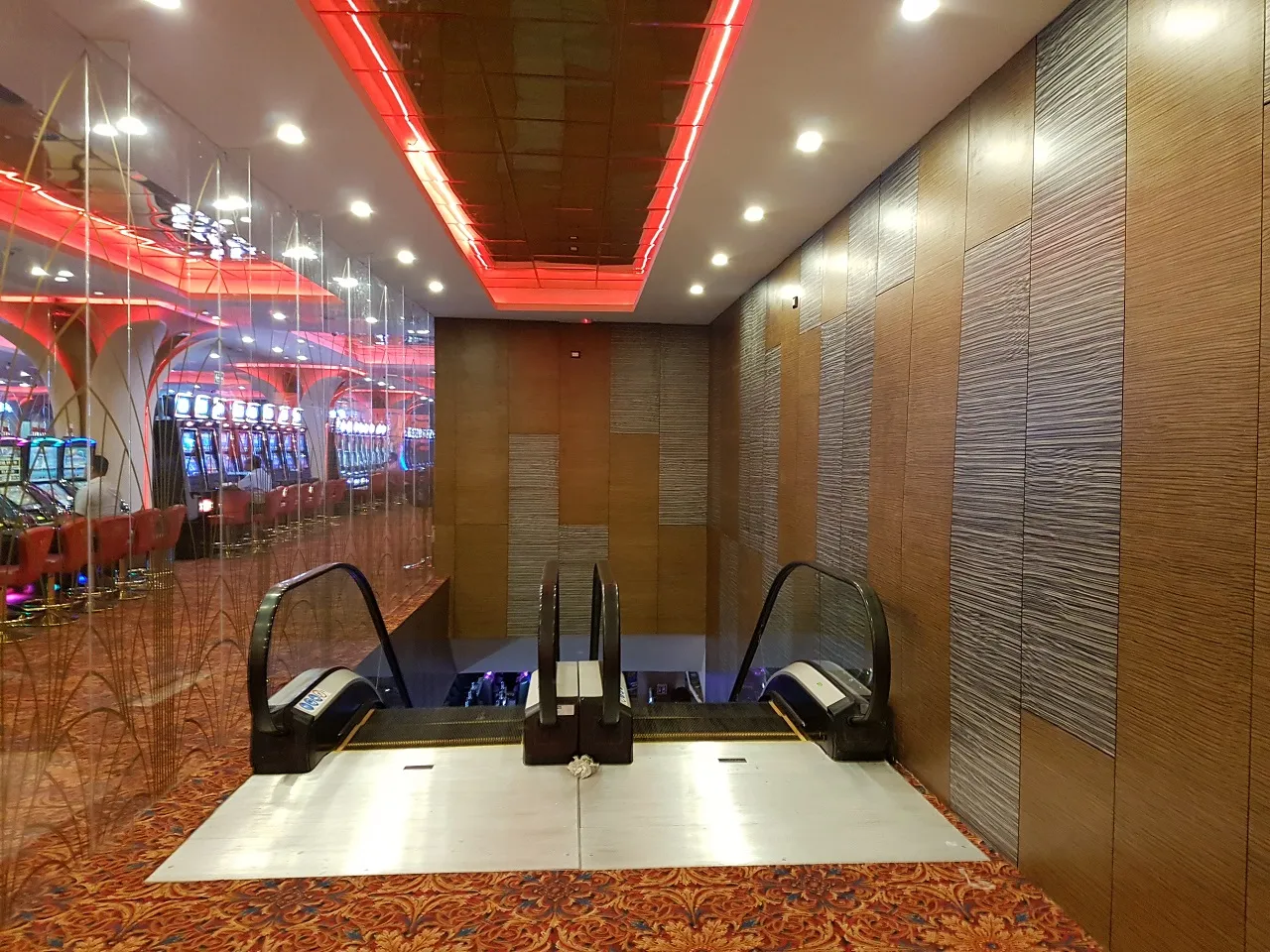 Vestíbulo del casino con muros recubiertos en madera y escaleras eléctricas.