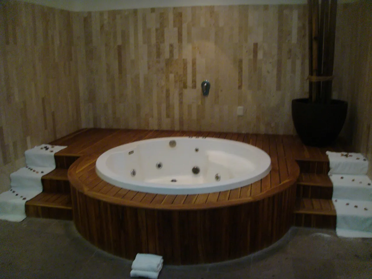 Jacuzzi con faldón y escalones de madera tropical, junto a un muro de piedra.