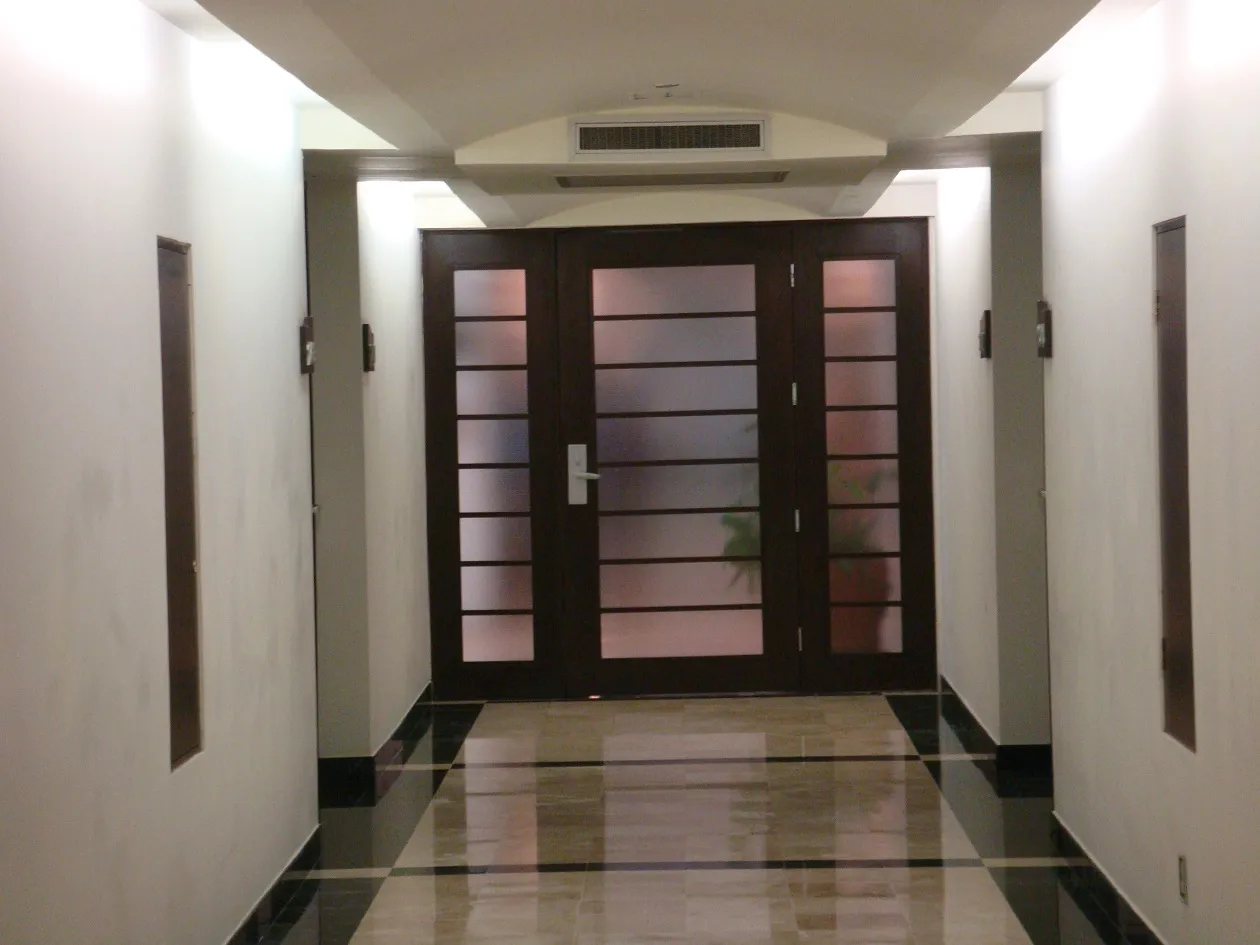 Pasillo del hotel con puerta doble de madera y vidrio, sobre piso de piedra pulida.