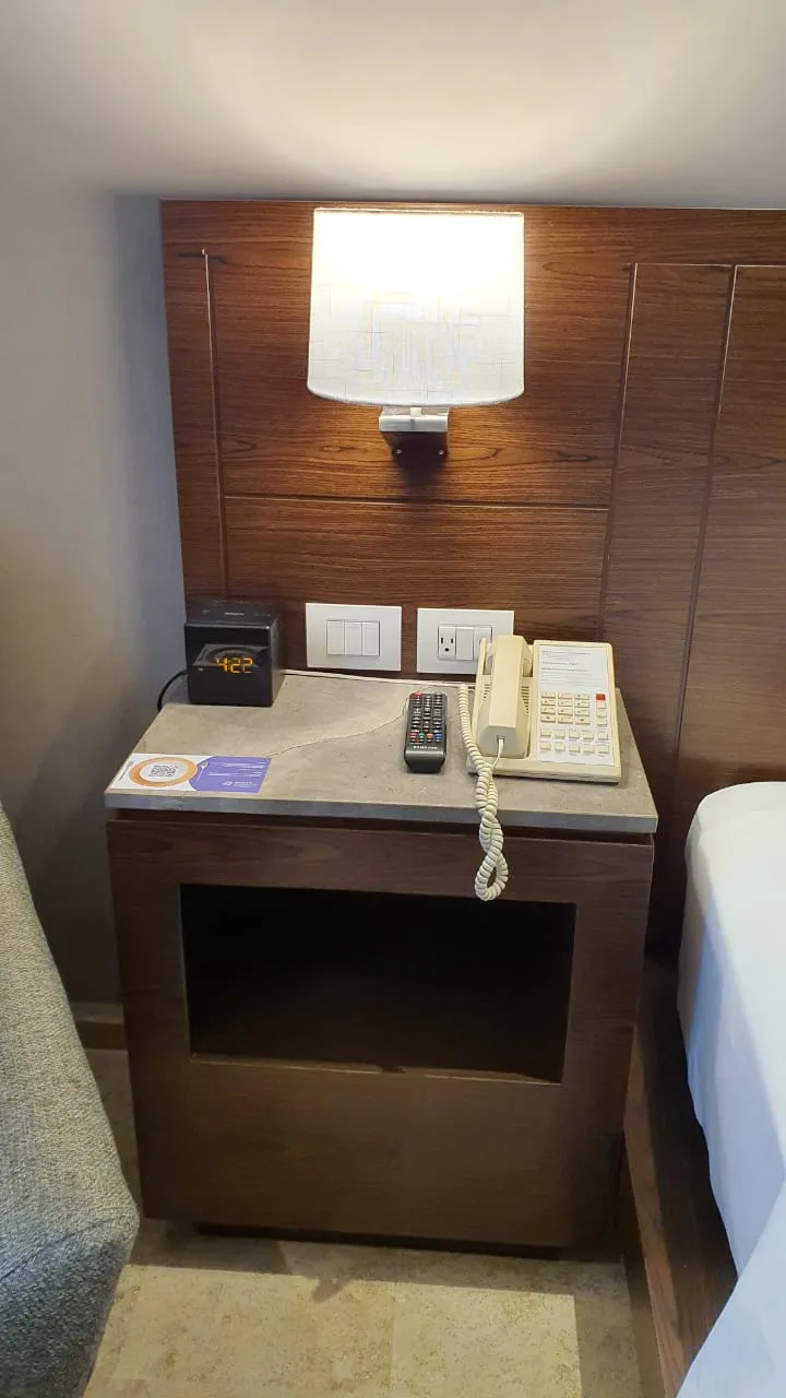 Buró de madera con cubierta de piedra y nicho abierto, contra un panel de madera con lámpara de pared, en una habitación del hotel.