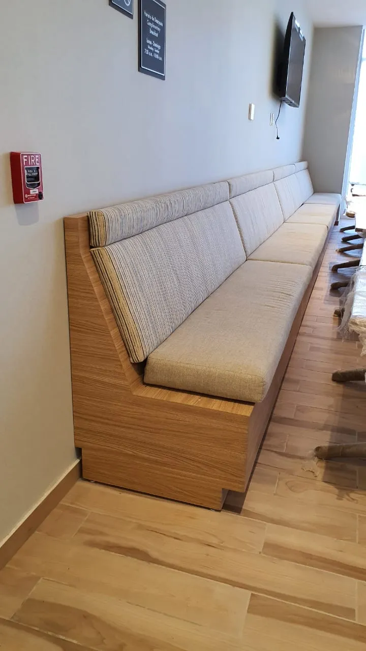 Banca corrida de madera clara a lo largo de un muro, en un área común del hotel.