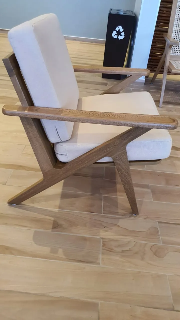 Butaca de madera con asiento tapizado en blanco, sobre piso de duela.